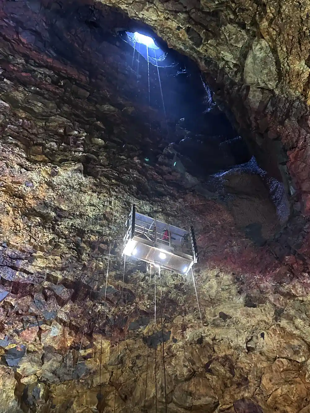 The lift platform suspended in the shaft, lit, seen from the floor