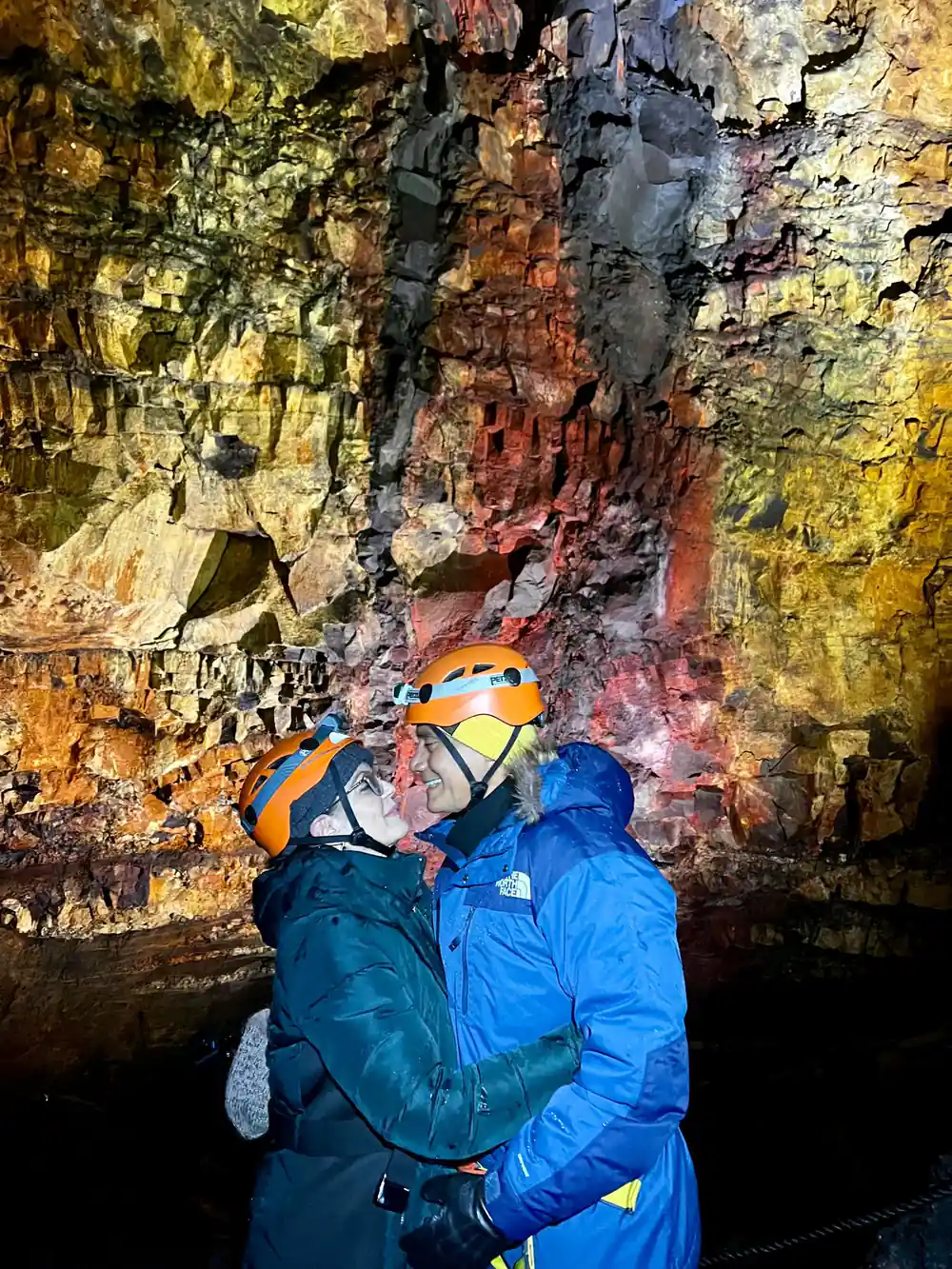 Two visitors in helmets against a wall of orange and red
